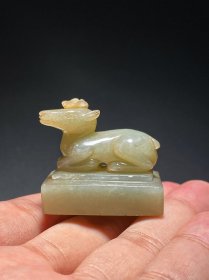 明 和田玉籽料 白玉 鹿钮 玉印 把件 挂件 长：3.5宽：2.2 高：3.3厘米 重：37.7克 印章为籽料玉质，局部褐色沁纹。印体为瘦长型长方体，印章钮圆雕成一鹿，鹿四肢屈于身下，侧首，角顶灵芝，头顶凸起，为“珍珠盘”，耳朝上，躯体健壮，二目圆睁，双耳后贴，雕工细致，肌肉，脚趾都雕刻清晰，并以阴刻线饰以毛发，腹部与印章间一孔便于佩戴把玩。