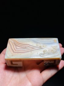 清 雨花玛瑙 缠丝玛瑙 春江泛舟 墨床 笔搁 摆件 长10.3 宽5 高3.2厘米 重228.7克 此件墨床书卷型，材质莹润，宛若云霞；墨床上面雕春江泛舟图，落“文玩”款，意境清幽，刀工遒劲，置于案头既是架搁墨锭的实用器具，同时也是赏心悦目的文房雅玩。