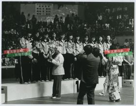 1981年11月16日在日本大阪进行第三届女排世界杯中，中国女排战胜日本队成为冠军。颁奖典礼中，孙晋芳代表全队接过奖杯，站在她旁边的是郎平。1981年银盐老照片一张，22.8X17.8厘米。