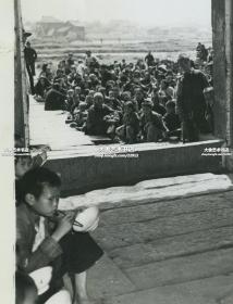 1946年湖南饥荒时期，原来的鱼米之乡不复存在，灾民儿童在赈灾中心吃着由UNRRA(联合国善后救济总署)提供的定量大米老照片。门外还有大量成人拿着碗，翘首以待进入吃饭。墙上贴有标语“要自立更生不要苟且偷安”，“推己及人  爱人以己”。22.8X18厘米