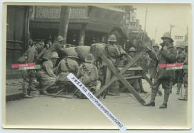 1932年淞沪抗战期间，驻守在上海公共租界的英国士兵驻守在路障之后，守卫在租界入口老照片，附近可见“源记号”商铺以及当铺标志牌等。15.1X10.1厘米，泛银