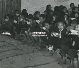 1946年湖南饥荒时期，原来的鱼米之乡不复存在，灾民儿童在赈灾中心吃着由UNRRA(联合国善后救济总署)提供的定量大米老照片。门外还有大量成人拿着碗，翘首以待进入吃饭。墙上贴有标语“要自立更生不要苟且偷安”，“推己及人  爱人以己”。22.8X18厘米
