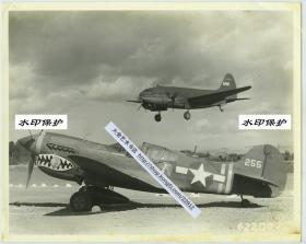 1940年代美国志愿援华航空队飞虎队驻华空军基地，鲨鱼头标志P40战斗机与起降中的C46大型运输机合影，战斗机上贴有五枚日寇海军旗标志，意味着它击落过五架日本战斗机。可能拍摄于云南昆明一带基地。25.2X20.2厘米