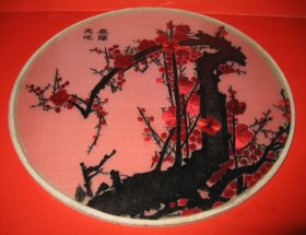 【春归天地：上世纪八十年代苏绣小品】圆形画幅，一树梅花，黑红双色调，黑为枝干红为梅，题名“春归大地”。双玻璃前后镶嵌密封，直径20.0厘米，厚0.5厘米。 背景为红色，图案主体是黑色和红色的梅花树枝。黑色的枝干和红色的梅花在红色背景的衬托下显得尤为醒目，展现了梅花傲雪凌霜的精神。在画幅左上角题名“春归天地”，传达了春天到来、万物复苏的意境。整个刺绣作品精致细腻，色彩搭配鲜明，具有浓厚的传统文化气息