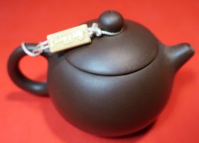 【西施壶：中国重汽曼技术发动机厂特别定制紫砂壶】西施壶。江苏宜兴黄龙山紫泥料。整壶通高9.0厘米，通长13.0厘米；口直径5.0厘米，腹直径9.0厘米，底足直径5.0厘米。质量205.0克。壶象丰满，流短而略粗，倒耳形壶柄，盖采用截盖式，壶底近底处内收。壶身钤字款“曼技术发动机厂”；壶底钤印“中国宜兴”，带作品收藏证书和原包装锦盒。