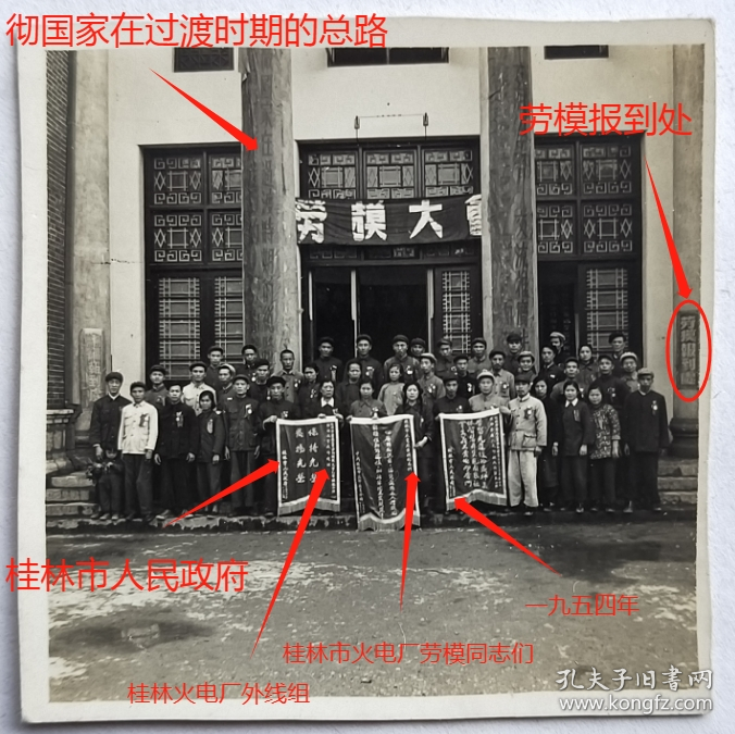 老照片：广西桂林，1954年“劳模大会”，桂林火电厂代表合影，锦旗上有“桂林市人民政府”，依稀可见“桂林市火电厂劳模同志们”、“桂林火电厂外线组”、“一九五四年”等字样，会场外面有“贯彻国家在过渡时期的总路线”标语，有“劳模报道处”指示牌。
