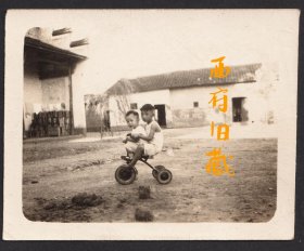 五十年代或民国老照片，独自在大院草地上骑着儿童车玩耍的小兄弟