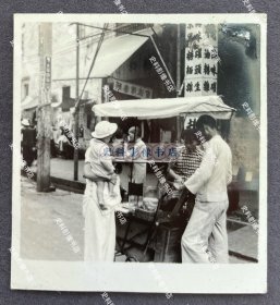 【广州旧影】1940年 广州沿街集市上推着带蓬小车售卖商品的小贩和抱孩子的旗袍少妇顾客 原版老照片一枚（可见沿街的“京味 海味 油糖 罐头 糖面…”、“…烟波室”等字样招牌，照片背面有1940年5月27日“广州中央宪兵分队”检阅章。）