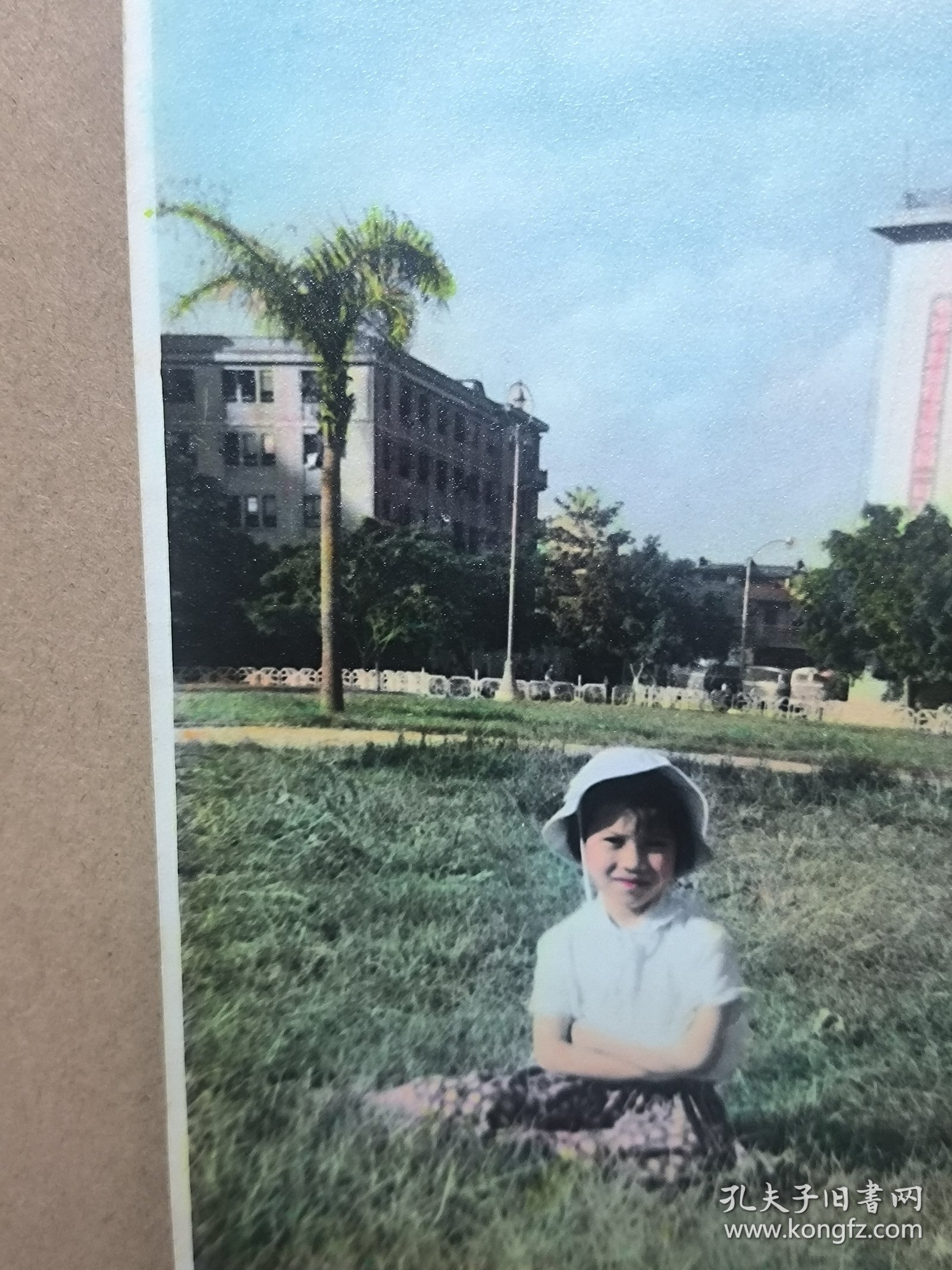 约60-70年代上色老照片一张 在广州海珠广场附近草坪留影，背景隐约有特色标语