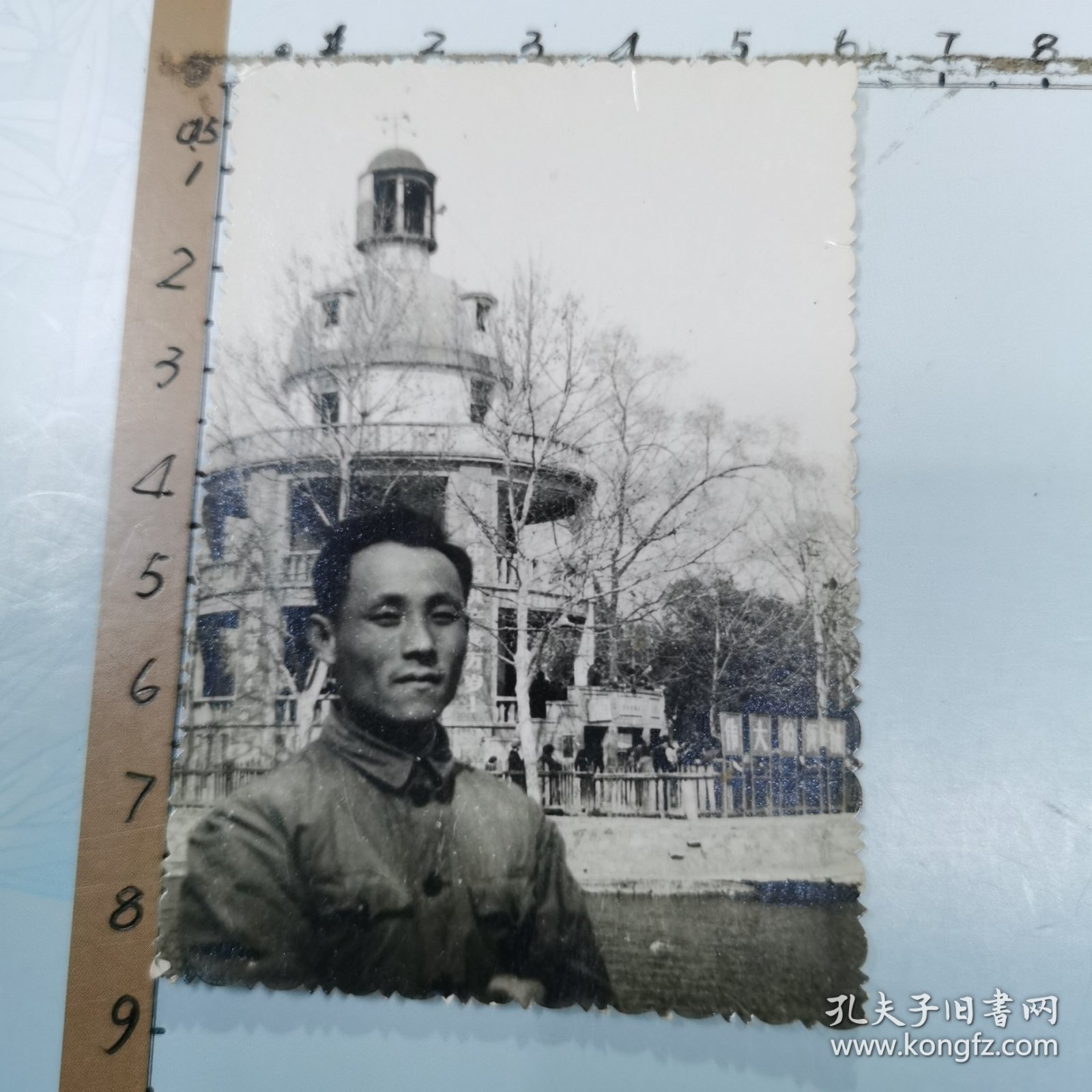 老照片：一位男士在武汉中山公园留影、背景是：“张公亭”廊柱上悬挂“伟大的中国共产党万岁、世界人民大团结万岁”布标、尺寸：6×8.5cm