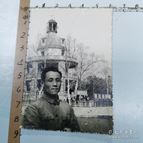 老照片：一位男士在武汉中山公园留影、背景是：“张公亭”廊柱上悬挂“伟大的中国共产党万岁、世界人民大团结万岁”布标、尺寸：6×8.5cm
