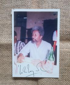 世界文化名人珍贵签名照～沃莱·索因卡，响誉世界的尼日利亚剧作家、诗人、小说家、评论家。1986年获诺贝尔文学奖，成为第一位获此殊荣的非洲作家。沃莱·索因卡在酒馆亲笔签名，双面签名（极罕见），带原签名证书，彩色，背面四个角有原来旧粘痕。尺寸12.8cmx8.9cm，品相好。