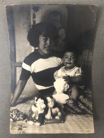 1950年母子二人在家中床上留影特色老照片（小男孩把玩着瓷雕像和玩具，后面贴着儿童宣传画）