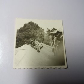 老照片–三名青年坐在景区山岩上留影（右侧亭子和游客清晰可见）