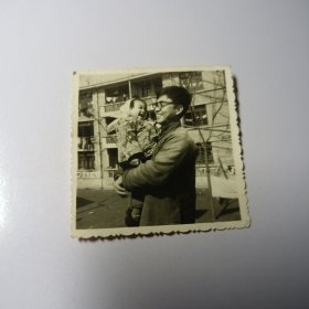 老照片–70年代初年轻父亲怀抱女儿在室外留影（1970年2月，二人笑的很开心，身后老建筑清晰可见）