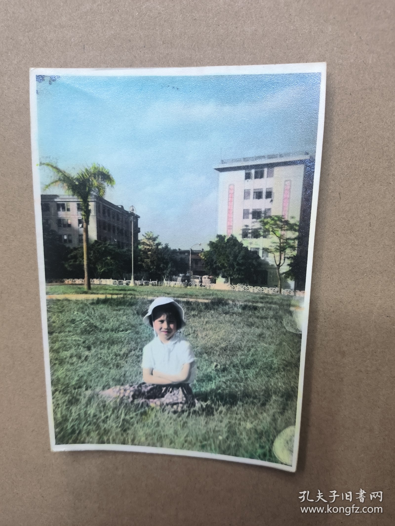 约60-70年代上色老照片一张 在广州海珠广场附近草坪留影，背景隐约有特色标语