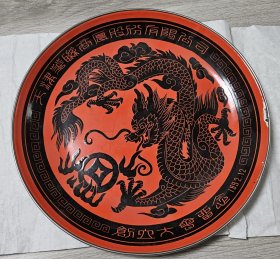 90年代彩绘搪瓷龙纹圆盘(天津华联商厦股份有限公司创立大会留念1992.12) 直径约37cm，天津搪瓷公司技校校办工厂绘制。整体保存很好，盘内边缘有小块碰损。 盘面中央绘有黑色龙纹图案，盘边装饰有精美花纹。整体为红色，龙纹红黑相间。龙纹图案威严生动，盘边文字清晰，体现传统工艺水平。 龙纹圆盘可作为礼品或装饰品，寓意富贵吉祥。