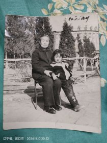 黑白照片营口县站前火车站广场祖孙二人合影，后面是振兴百货商店
