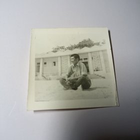 老照片–80年代青年坐在景区沙滩上留影（身后有一座建筑）