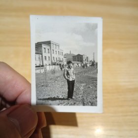 老照片–男子站在室外空地上留影（身后老建筑和行人清晰可见）