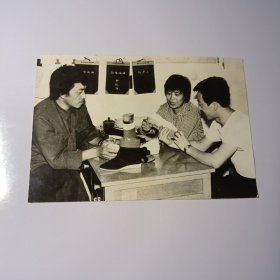 老照片–80年代三名青年坐在办公桌前观看鞋子留影