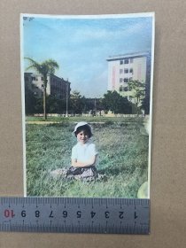 约60-70年代上色老照片一张 在广州海珠广场附近草坪留影，背景隐约有特色标语