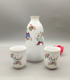 日本深川制瓷酒具一套，精美婴戏纹样，酒壶配2个酒盅，壶身绘制可爱小孩采菊图，釉色纯正自然。壶身白瓷胎，金边装饰，保存完好。底部有深川制款，做工精致。壶肚径5.5厘米，高13.5厘米。杯口径4.5厘米，高5.5厘米。