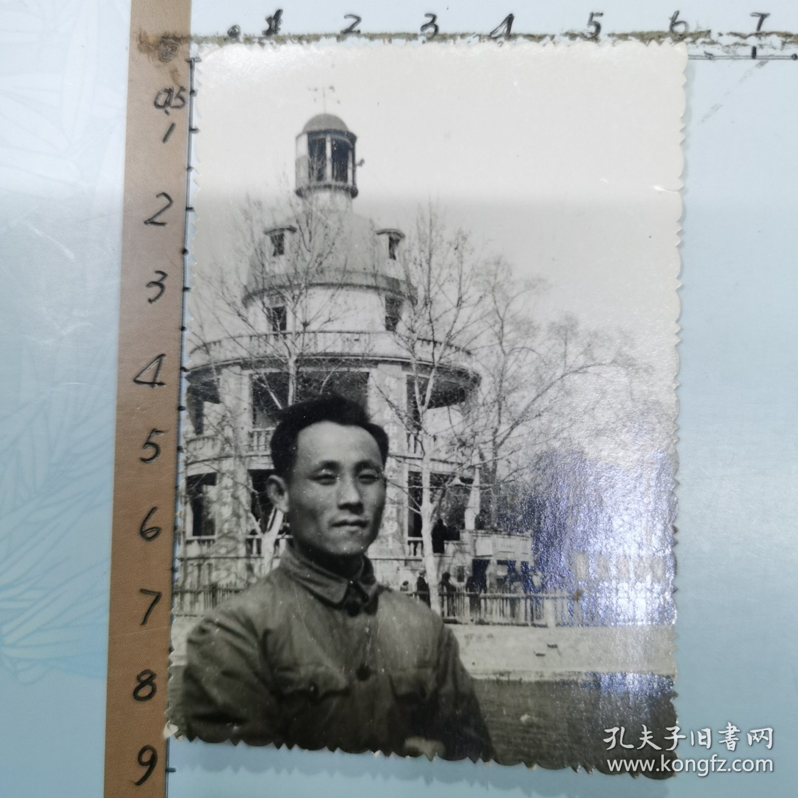 老照片：一位男士在武汉中山公园留影、背景是：“张公亭”廊柱上悬挂“伟大的中国共产党万岁、世界人民大团结万岁”布标、尺寸：6×8.5cm