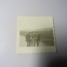 老照片–四名青年在乡村路上留影（身旁有一辆自行车，身后田地和山坡清晰可见）