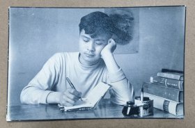 约60年代黑白老照片一张 青年学子可能大学生 在书桌前提着钢笔写字 旁边有墨水盒和一沓课本 相纸质量优良，拍摄清晰