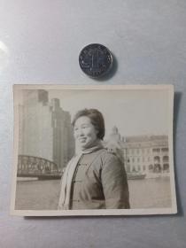 1970年代，一位妇女在上海黄浦江和苏州河交汇处的黄浦公园内，背景为上海大厦、外白渡桥和苏联驻沪总领事馆
