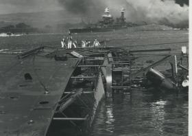 1941年12月7日日本偷袭美国太平洋海军舰队珍珠港老照片，基地一片惨状，近景的舰只已经倾覆沉没，远处的巡洋舰燃起滚滚黑烟。。