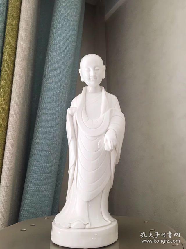 白瓷微笑小佛陀，家居装饰佳品，带包装 此艺术品为白瓷，瓷雕表面白洁如玉，衬托以小沙弥佛性的微笑，佛陀面部刻画俊朗，面部轮廓甜美，俊雅，展现东方式的迷人微笑，渡人向善，让欣赏者心灵受到净化变得安静纯净。尺寸高约35cm，肩宽约11cm。