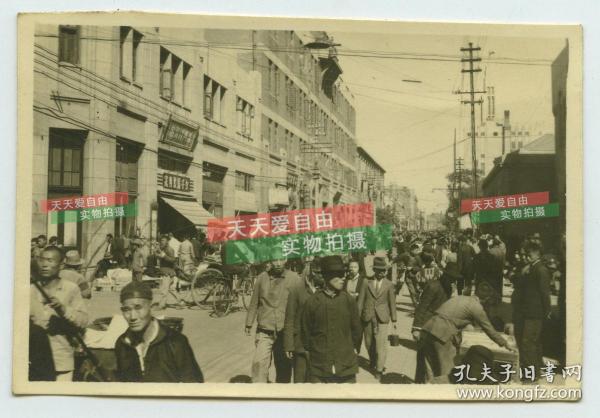 民国1945年左右天津和平路人流熙攘的街道，可见远处中原公司的尖顶，新兴洋服店女子服装专家等招牌。泛银