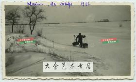 1935年冬季天津冰封的原野，有百姓挑着筐出行，在雪地中留下一排长长的足迹。民国老照片一张。